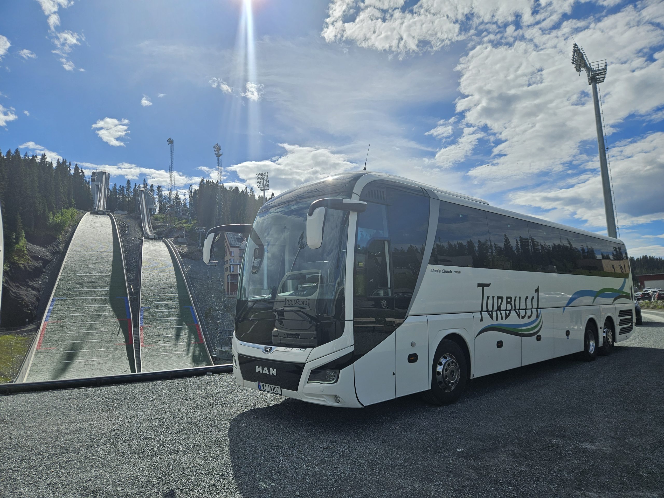 Turbuss1 turbuss parkert ved idrettsanlegg en sommerdag